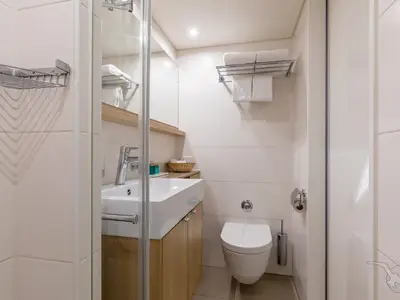 Helles Badezimmer an Bord der MS Adora. Zu sehen sind ein weißes Waschbecken, ein Holzunterschrank, eine Toilette und eine verchromte Handtuchablage mit weißen Handtüchern.