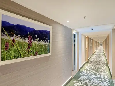 Ein langer, heller Flur an Bord der MS Alena mit grün-weißem Blumenteppich. An der Wand hängt ein großes Bild mit Alpenlandschaft.