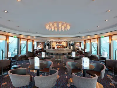Innenansicht der Panorama Bar auf der MS Alina. Eine zentrale runde Bar, umgeben von eleganten Tischen und Sesseln. Große Fenster bieten Weitblick.