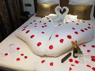 Romantisch dekorierte Kabine an Bord der MS Alina. Bett mit roten Rosenblättern, Champagnerflaschen, Gläsern und zu Schwänen gefalteten Handtüchern.