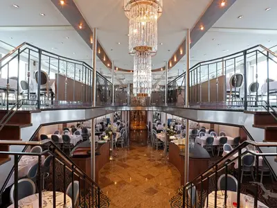 Ein großzügiges Restaurant auf der MS Alina, erstreckt sich über zwei Ebenen mit Tischen und Stühlen, gekrönt von einem imposanten Kristall-Kronleuchter.