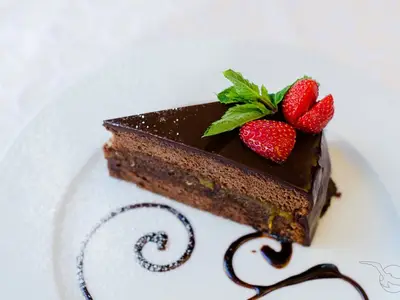 Detailaufnahme eines Schokoladenkuchens mit Glasur, garniert mit Erdbeeren und Minze, an Bord der MS Alina. Der Teller ist mit Puderzucker und Schokoladensauce verziert.