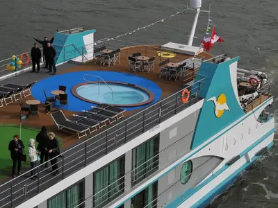Das Sonnendeck der MS Alina von oben: Whirlpool, Liegestühle und Tische für Gäste. Ein Putting Green ist ebenfalls zu sehen. Am Heck weht eine rote Flagge des fahrenden Flussschiffes.