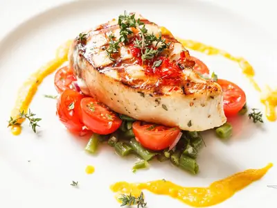 Ein appetitliches, gegrilltes Wolfsbarschfilet, garniert mit Kräutern und Chilis, auf grünen Bohnen und Kirschtomaten mit gelber Sauce, serviert an Bord der MS Alina.