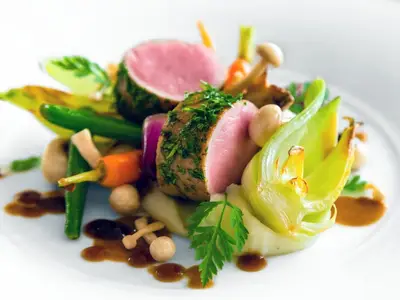 Nahaufnahme eines elegant angerichteten Hauptgerichts an Bord der MS Alina. Rosa gebratenes Schweinefilet mit frischem Gemüse wie Karotten, Bohnen, Pilzen und Paprika, dazu dunkle Sauce auf weißem Teller.