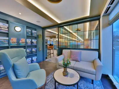 Helle, moderne Lounge an Bord der MS Alisa mit bequemen Sesseln, Sofa und Bücherregalen. Ein Fensterbereich grenzt an eine Bar und gibt den Blick nach draußen frei.