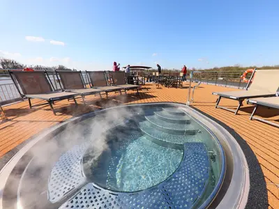 Das sonnige Sonnendeck der MS Alisa mit dampfendem Whirlpool, Liegestühlen und Tischen. Mehrere Passagiere und Flusslandschaft im Hintergrund.