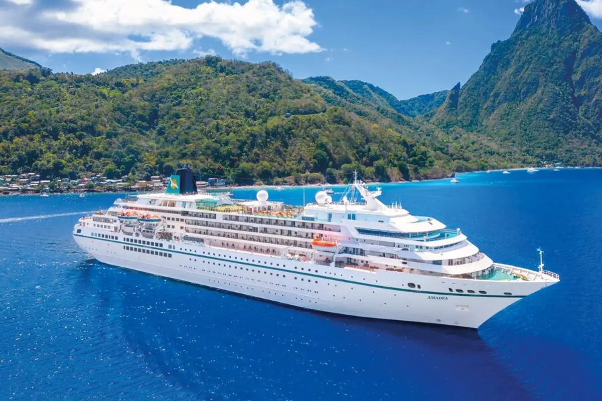 Die MS Amadea in einer malerischen tropischen Bucht, umgeben von üppig grünen Bergen und tiefblauem Meer unter strahlend blauem Himmel. Eine idyllische Szenerie.
