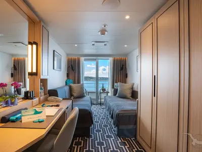 Eine helle und moderne Balkonkabine an Bord der MS Amadea mit zwei Betten, einem Schreibtisch und einem großen Fenster zum Meer.