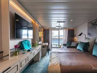 Helle Balkonkabine an Bord der MS Amadea mit Doppelbett, Sofa und Schreibtisch. Die Balkontür öffnet den Blick auf Meer und Himmel.
