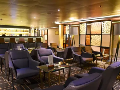 Elegante Kopernikus Bar an Bord der MS Amadea. Eine beleuchtete Bar mit Flaschen, Hockern, sowie bequeme Sessel und Glastische füllen den Raum.