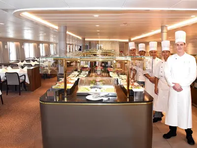 Blick auf das reichhaltige Buffet im Restaurant Amadea mit mehreren lächelnden Crewmitgliedern in Kochuniformen an Bord der MS Amadea.