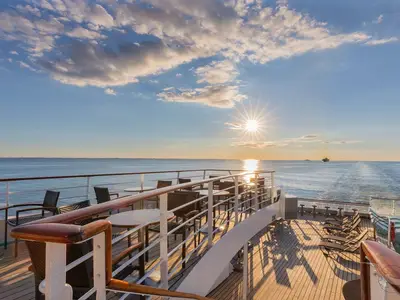 Sonnenuntergang auf dem Sonnendeck der MS Amadea. Das Holzdeck ist mit Tischen, Stühlen und Liegestühlen ausgestattet, mit Blick auf das weite Meer.
