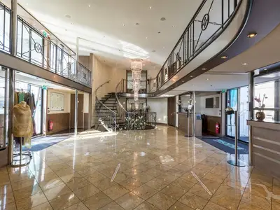 Das elegante Atrium der MS Amelia: imposante Wendeltreppe, großer Kristallkronleuchter, glänzende Marmorböden. Helles Tageslicht flutet den stilvollen Raum.