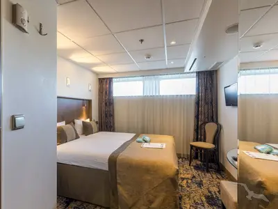Außenkabine an Bord der MS Amelia. Zwei Einzelbetten, gemusterte Vorhänge, große Fenster, ein Stuhl und ein Wand-TV sind zu sehen. Die Kabine ist hell beleuchtet.