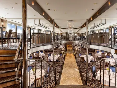 Blick von oben in das elegante, zweistöckige Restaurant Loreley an Bord der MS Amelia. Gedeckte Tische mit blauen Stühlen, Treppen, ein Kronleuchter und Fensterbereiche sind zu sehen.