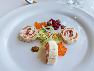 Eine Nahaufnahme einer eleganten Vorspeise mit Lachsrollen, Frischkäse, rotem Kaviar und frischem Salat auf einem weißen Teller an Bord der MS Amelia.