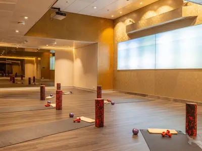 Ein moderner Fitnessraum an Bord der MS Amera. Yoga-Matten, Foam-Roller und Hanteln liegen bereit. Verspiegelte Wand und große Bildschirme mit Meerespanorama.