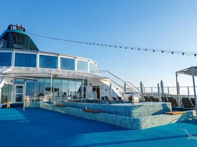 Die MS Amera präsentiert ihr sonniges Oberdeck mit einem blauen Pool, bequemen Liegestühlen und einem modernen Glasgebäude unter blauem Himmel.