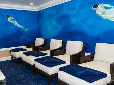 Blick in einen hellen Entspannungsbereich an Bord der MS Amera. Die Wände zeigen eine blaue Unterwasser-Wandmalerei. Mehrere Liegestühle mit weißen Polstern und blauen Decken laden zum Verweilen ein.