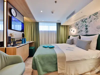 Eine geschmackvolle Außenkabine an Bord der MS Amina. Ein großes Bett mit floraler Tapete, ein Arbeitsbereich mit TV und Fenster laden zum Entspannen ein.