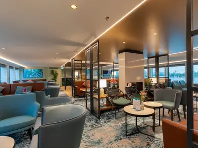Geräumige, modern eingerichtete Bar-Lounge an Bord der MS Amina mit verschiedenen Sitzbereichen, großen Fenstern und indirekter Beleuchtung. Blick auf einen Fluss und Bäume.