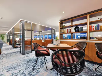 Eine modern gestaltete Panorama-Lounge an Bord der MS Amina mit bequemen Sitzgelegenheiten, Tischen und einer Bücherwand. Große Fenster bieten einen weiten Blick auf die Landschaft.