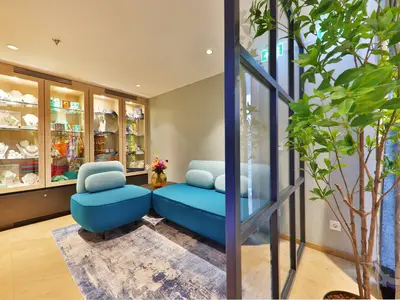 Ansicht eines hellen Shops an Bord der MS Amina. Mehrere beleuchtete Vitrinen präsentieren Schmuck und Accessoires. Im Vordergrund moderne blaue Sofas und ein kleiner Beistelltisch mit Blumenvase, abgetrennt durch eine Glaswand mit Pflanzen.