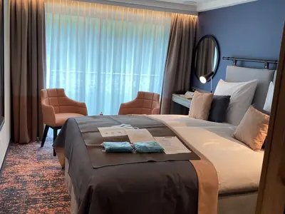Gemütliche Außenkabine an Bord der MS Andrea. Ein Doppelbett mit Willkommens-Päckchen, daneben zwei rosa Sessel vor dem Fenster. Ein Spiegel und eine Leselampe sind sichtbar.