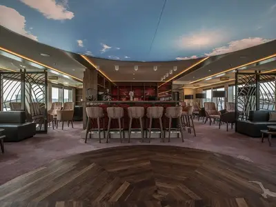 Elegante Bar-Lounge der MS Andrea mit Theke, Barhockern und Sesseln. Große Fensterflächen bieten Flussblick. Die beleuchtete Decke zeigt einen Himmel mit Wolken und Sonne.
