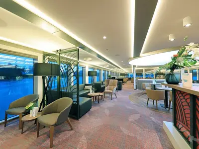 Weitwinkelansicht der eleganten Bar-Lounge an Bord der MS Andrea. Helle, moderne Einrichtung mit bequemen Sitzgruppen und einem großen Fensterbereich mit Blick nach draußen.