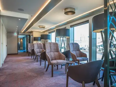 Eine geräumige Lounge an Bord der MS Andrea mit modernen Sesseln, großen Panoramafenstern und stimmungsvoller Deckenbeleuchtung.