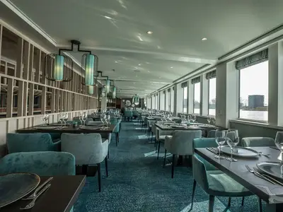Das elegante Restaurant der MS Andrea: Zahlreiche gedeckte Tische, teal-farbene Stühle und große Fenster mit Flussblick. Moderne Deckenlampen sorgen für stimmungsvolle Beleuchtung.