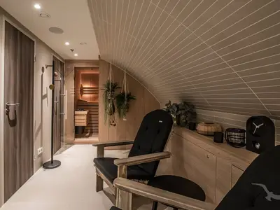 Ein stilvoller Wellnessbereich an Bord der MS Andrea mit einer holzverkleideten Sauna, bequemen schwarzen Ruhesesseln und hängenden Pflanzen. Die Decke ist schräg und gefliest, das Licht warm.