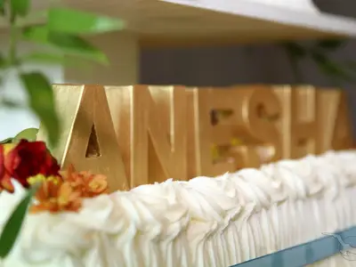 Nahaufnahme einer festlichen Torte an Bord der MS Anesha. Goldene 3D-Buchstaben bilden den Namen 'ANESHA' und sind von roten sowie orangen Blumen umgeben. Der Rand der Torte ist mit weißer Creme verziert.