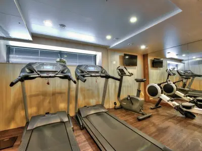 Fitnessraum an Bord der MS Anesha. Zwei Laufbänder, ein Hometrainer und Rudergeräte stehen bereit. Helle Holzwände und eine Spiegelwand erzeugen ein offenes Raumgefühl.