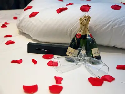 Nahaufnahme einer romantisch dekorierten Kabine an Bord der MS Anesha. Zwei Flaschen Moët & Chandon Champagner, zwei leere Gläser und rote Rosenblätter liegen auf dem weißen Bettlaken.