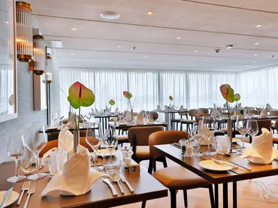 Elegantes Restaurant an Bord der MS Anesha. Helle Einrichtung, gedeckte Tische mit Blumendeko und großen Fenstern. Ohne Personen.