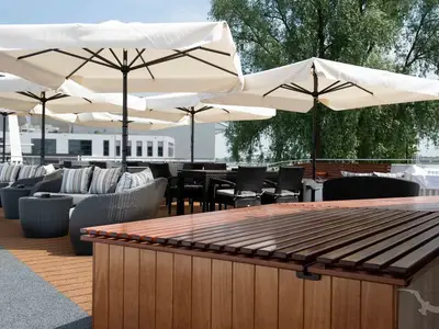 Das Sonnendeck der MS Anesha mit gemütlichen Rattan-Sitzgruppen, gestreiften Kissen und großen Sonnenschirmen. Holz-Counter und Flussufer mit Bäumen im Hintergrund.