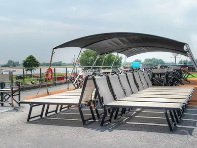 Das Sonnendeck der MS Anesha bei Tageslicht zeigt mehrere aufgestellte Liegestühle unter einem dunklen Sonnensegel. Im Hintergrund ist eine grüne Flusslandschaft mit Bäumen zu sehen. Ein Rettungsring hängt am Geländer.