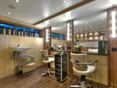 Ein heller, moderner Friseursalon an Bord der MS Anesha mit zwei Friseurstühlen, einem Haarwaschbecken und Regalen voller Produkte.