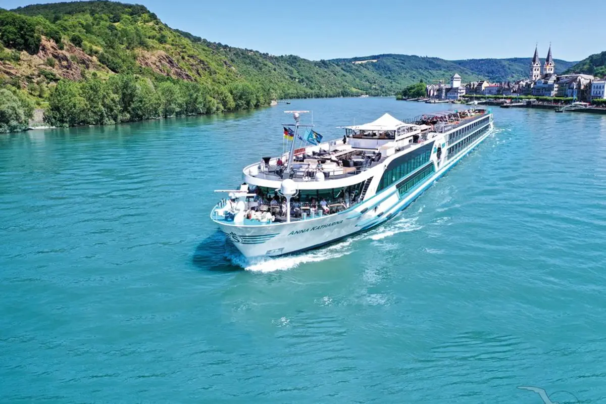 Luftaufnahme der MS Anna Katharina auf einem breiten Fluss, umgeben von bewaldeten Hügeln und einer malerischen Stadt mit Doppeltürmen.