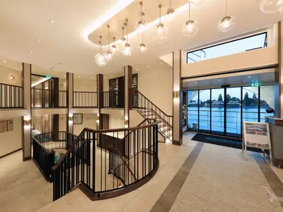 Helles Atrium an Bord der MS Anna Katharina. Elegante Treppen, Panoramafenster mit Blick auf den Fluss und Uferlandschaft. Modernes Design mit warmen Lichtern.