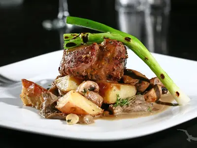 Nahaufnahme eines appetitlichen Steaks mit Pilzen, Kartoffeln und Frühlingszwiebel, serviert mit Soße auf einem weißen Teller an Bord der MS Anna Katharina.