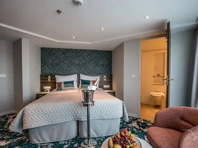 Blick in eine helle Kabine an Bord der MS Annabelle. Ein großes Doppelbett mit Nachttischen dominiert den Raum. Eine Flasche Champagner in einem Kühler steht bereit. Eine offene Tür führt zum Badezimmer mit Toilette.