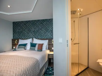 Ein modernes Schlafzimmer in einer Kabine an Bord der MS Annabelle mit Doppelbett, Nachttisch und angrenzendem Badezimmer mit Dusche und Glasschiebetür.