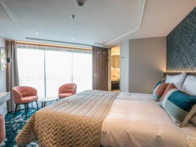 Helle, moderne Balkonkabine der MS Annabelle mit Doppelbett, Sitzbereich und großen Panoramafenstern. Das Badezimmer ist durch eine offene Tür sichtbar. Einladendes Ambiente.
