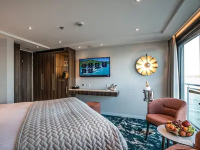 Eine elegant eingerichtete Balkonkabine an Bord der MS Annabelle mit einem bequemen Bett, einem TV, einem Schreibtisch und einem Balkon mit Flussblick.