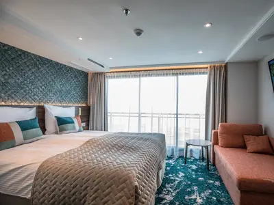 Eine helle, modern gestaltete Balkonkabine an Bord der MS Annabelle. Zu sehen sind ein Doppelbett mit bunten Kissen, ein bequemer Sitzbereich mit Couch und ein Fenster zur Aussicht. Der Boden ist mit einem teal-farbenen Teppich ausgelegt.