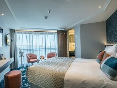 Helle, moderne Suite an Bord der MS Annabelle mit Doppelbett, zwei Sesseln und Balkonblick auf das Meer. Tisch mit Obst und Champagner. Einladende Einrichtung.